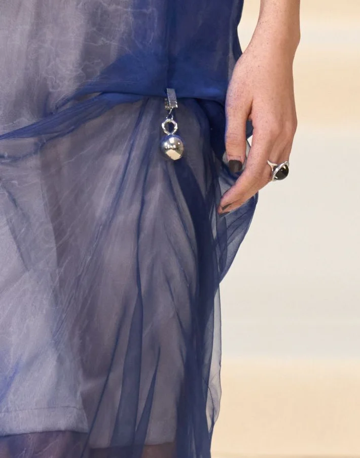 Closer: a small metal sphere on a clip at the hip, with the organza gathered towards it.