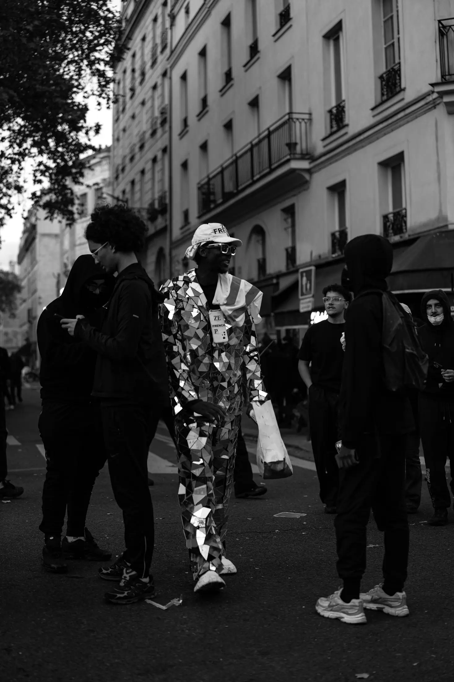 A protester in a suit of mirrored squares near Place de la République, holding a sign that reads 17 OCT 26.