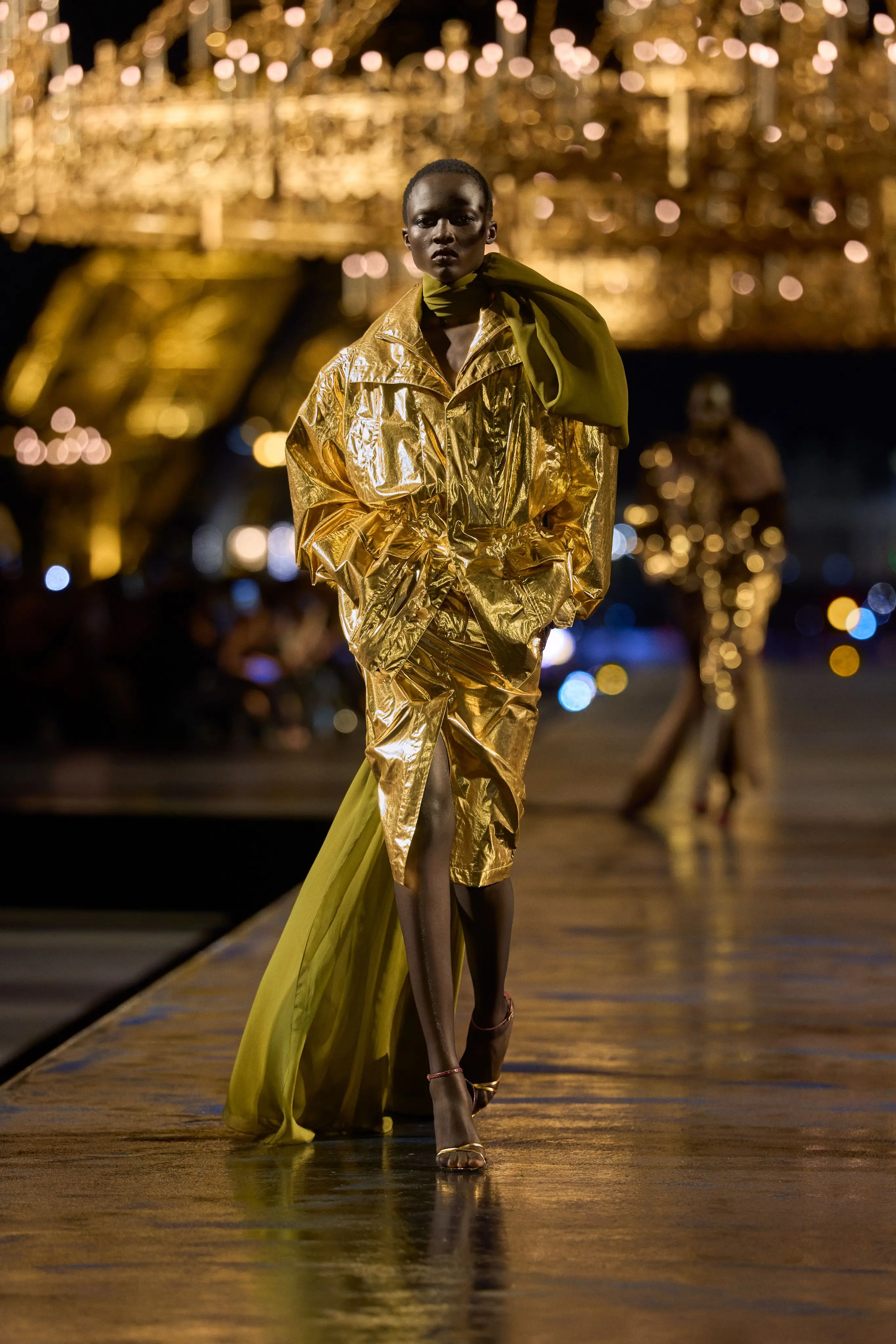 Saint Laurent SS27, Look 1. The opening look, in gold, under the chandeliers.